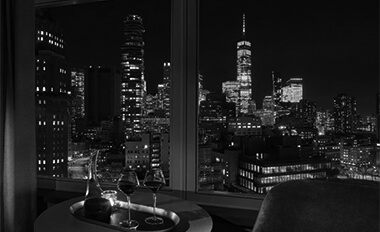 A hotel room table set with glasses, overlooking a city skyline at night