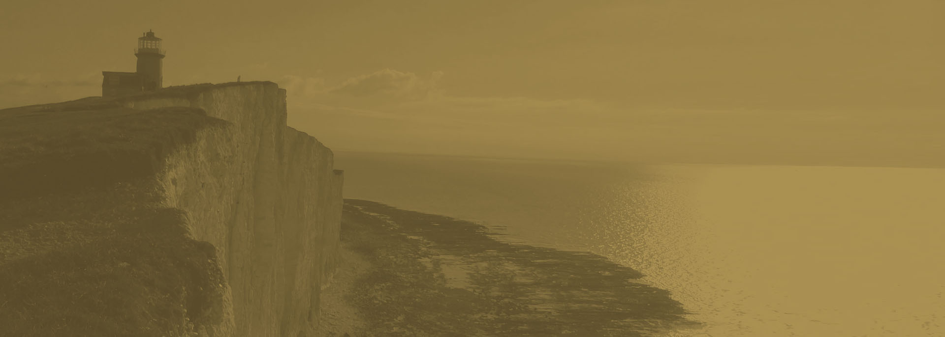 A lighthouse standing on chalk cliffs above the sea at dusk